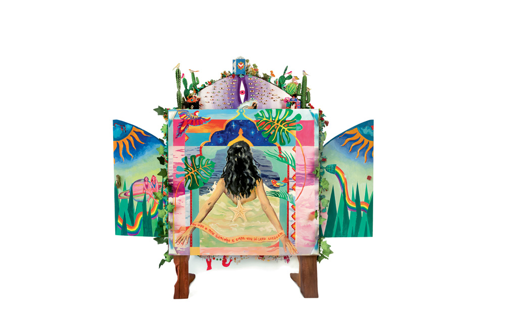 Oratório – VERSO com portas – Marcela Cantuária – foto Vicente de Mello.VDM_6475 2.jpg Oratório com portas é pintado bem colorido. Tem uma garota de costas no mar estampada. Há sóis, árvores, estrelas e outros elementos da natureza na arte