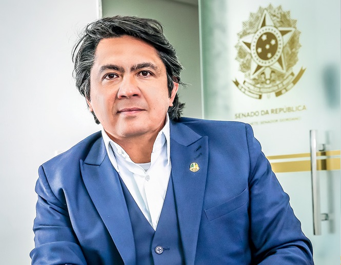 O senador Alexadre Giordano posa sentado em uma cadeira de terno azul e camisa social