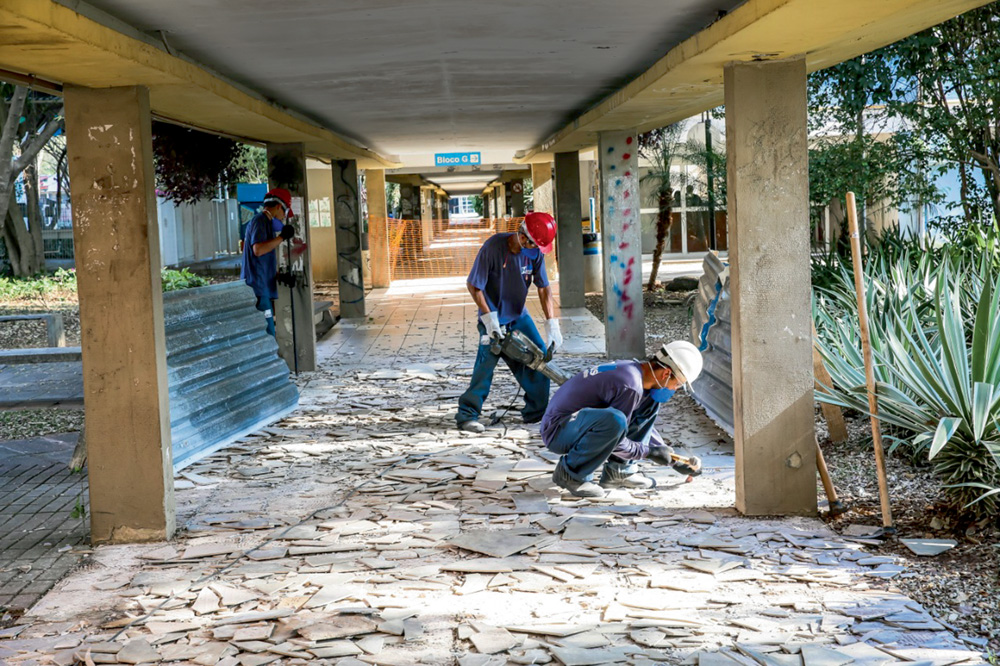 Passarela USP CRUSP Pedreiros trabalham no piso de uma obra, que é um vão sustentado por colunas de um prédio