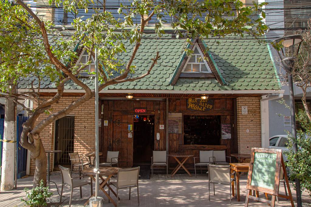 Fachada do bar Zur Alten Mühle, com telhadinho verde e parede de tijolos.