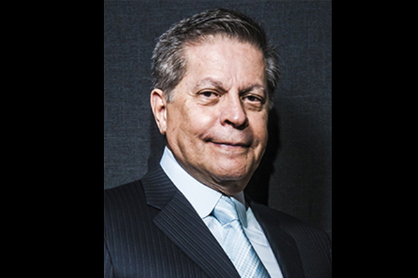 Imagem mostra Carlos Alberto de Oliveira sorrindo de terno em fundo escuro