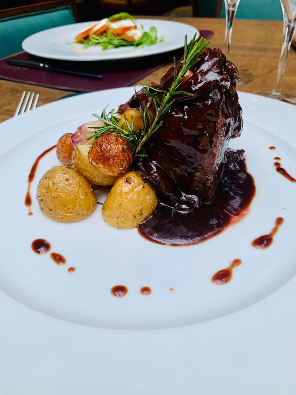 Attimo filetto tartufato file mignon com mix de cogumelos trufados e vinho Marsala DOC servido com batatas rusticas Prato branco com carne ao molho, batata e molho decorando ao redor