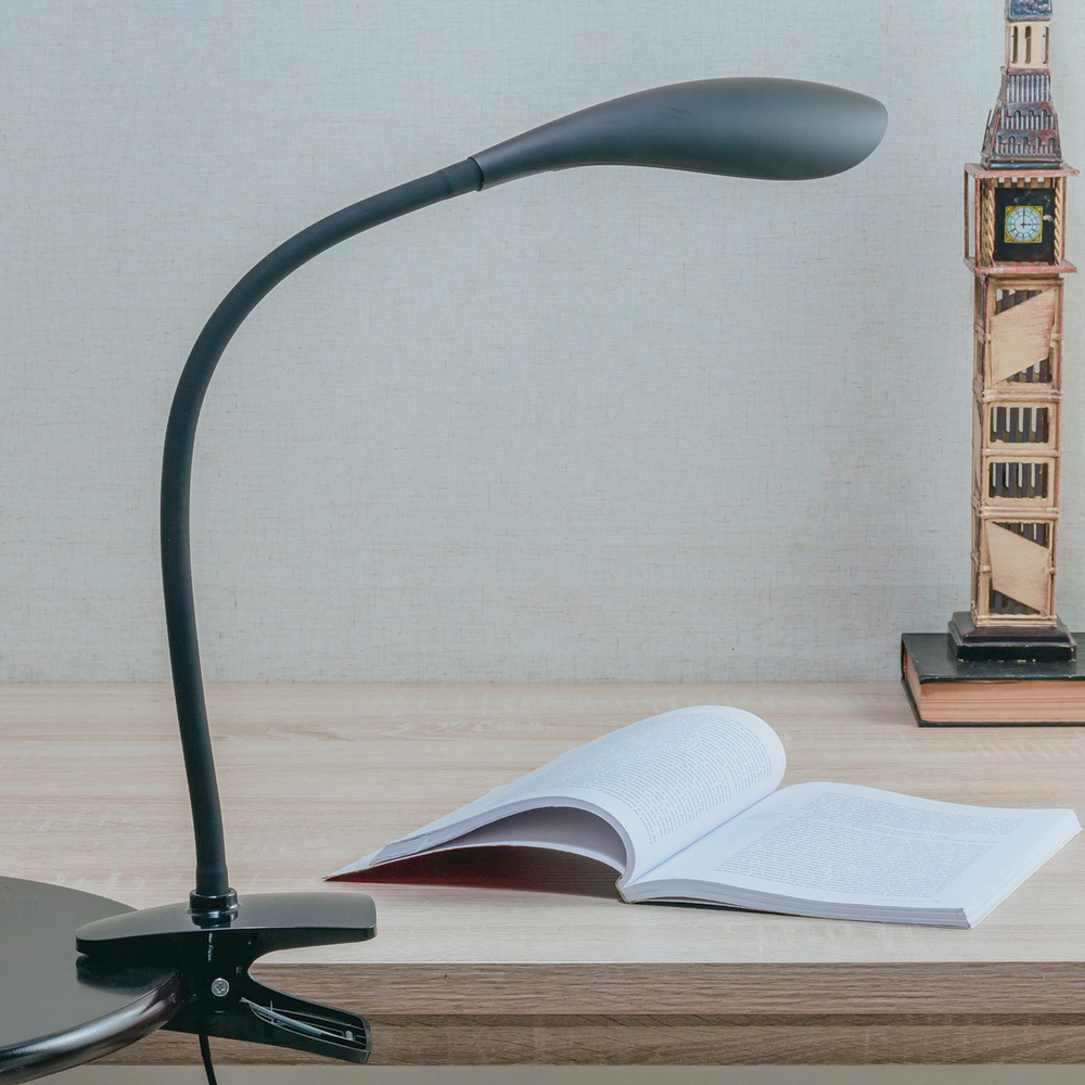 luminária clip.jpg Uma luminária preta simples em cima de uma mesa. Está iluminando um livro