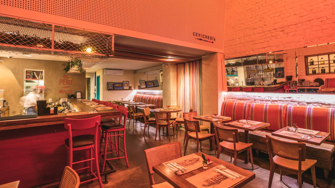 Ambiente do restaurante La Peruana de decoração colorida, com bancos altos de cor rosa e mesas e cadeiras de madeira
