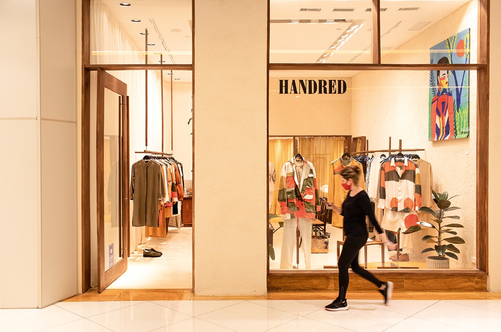 Fachada da loja da marca Handred no Shopping Iguatemi. A fotos tem tons laranjas e algumas roupas estão expostas na vitrine
