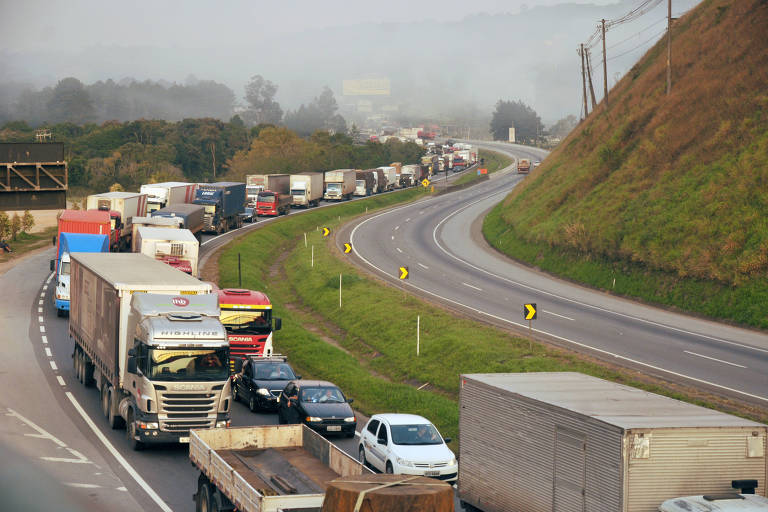 Imagem de pista lotada de caminhões parados.