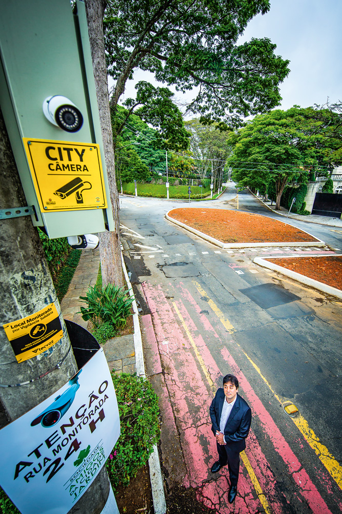 câmera-cidade-jardim-marcelo-reis-lobo-fracasso-projeto-city-câmeras-baixa-adesão-público-prefeitura-promete-repaginação foto tirada de cima, do advogado reis lobo olhando para a câmera, instalada em cima de um poste na rua, do projeto city câmeras, da prefeitura
