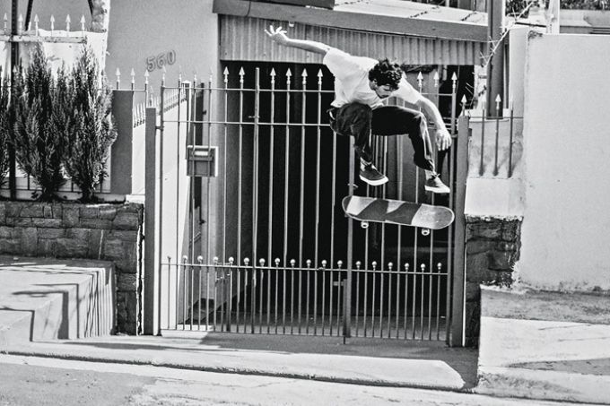 foto em preto e branco de Henrique Crobelatti fazendo manobra de skate no ar em uma rua residencial