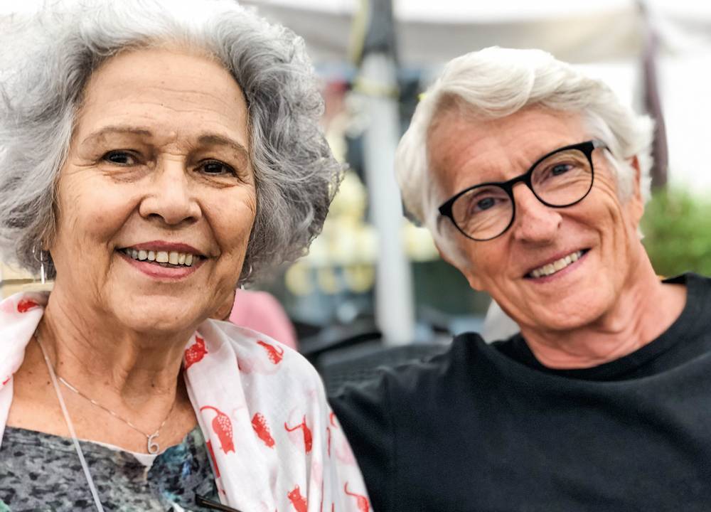 Mary Porto e Raymond Widmer um ao lado do outro, de cabelos brancos, sorrindo para a foto