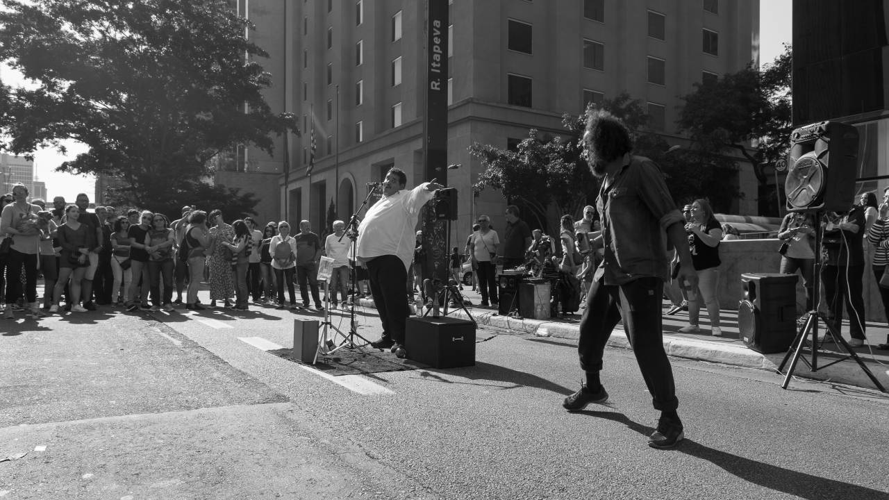 Tim Maia da Paulista se apresentando na Avenida Paulista, de pé, com microfone à frente