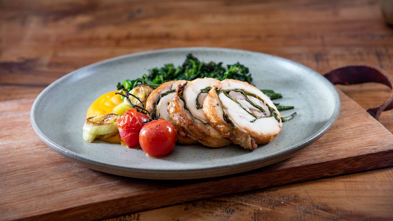 Prato de cerâmica azul com pedaços de frango de rolo, tomatinhos confitados e cebola.