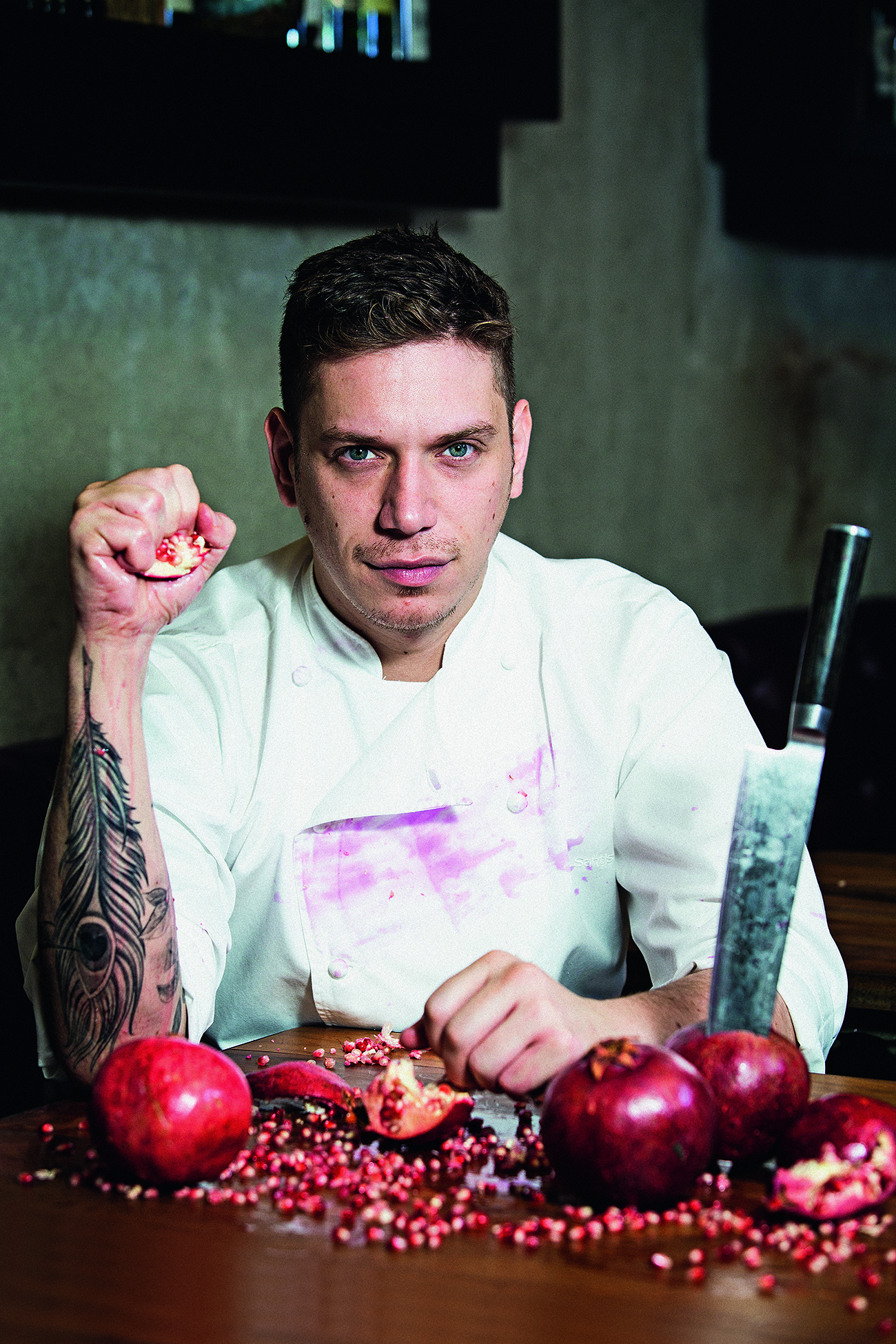 O chef Rodolfo DeSantis sento &agrave; mesa espremendo uma fruta com a m&atilde;o.