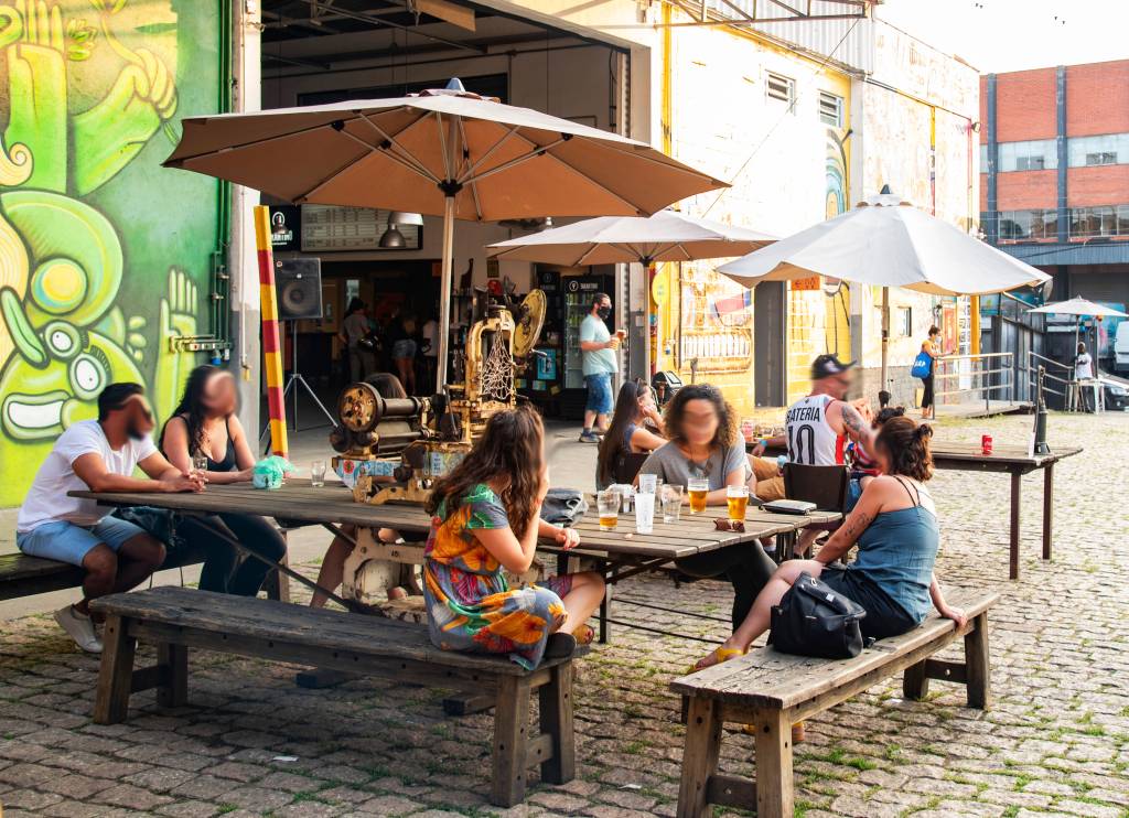 Espaço ao ar livre da Cervejaria Tarantino, com pessoas sentadas em mesa de madeira coberta por guarda-sóis.