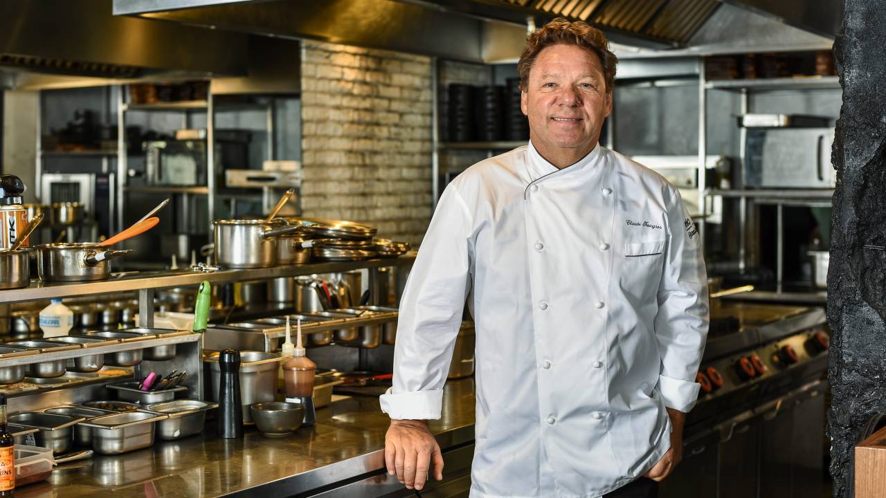 O chef Claude Troisgros de dólmã apoiado em bancada da cozinha do Chez Claude.