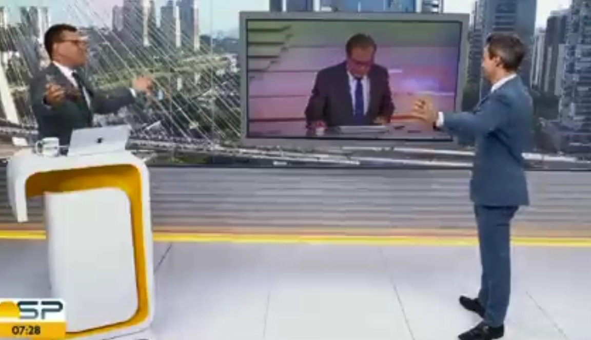 A imagem mostra dois apresentadores do Bom Dia SP, olhando para o telão onde está Chico Pinheiro sentado em um balcão, com os braços abertos
