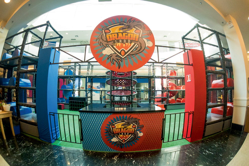 Dragon Land no Mooca Plaza Shopping (2).jpg Dentro de um shopping, uma estrutura colorida em vermelho e azul com tobogãs. Na entrada, a placa