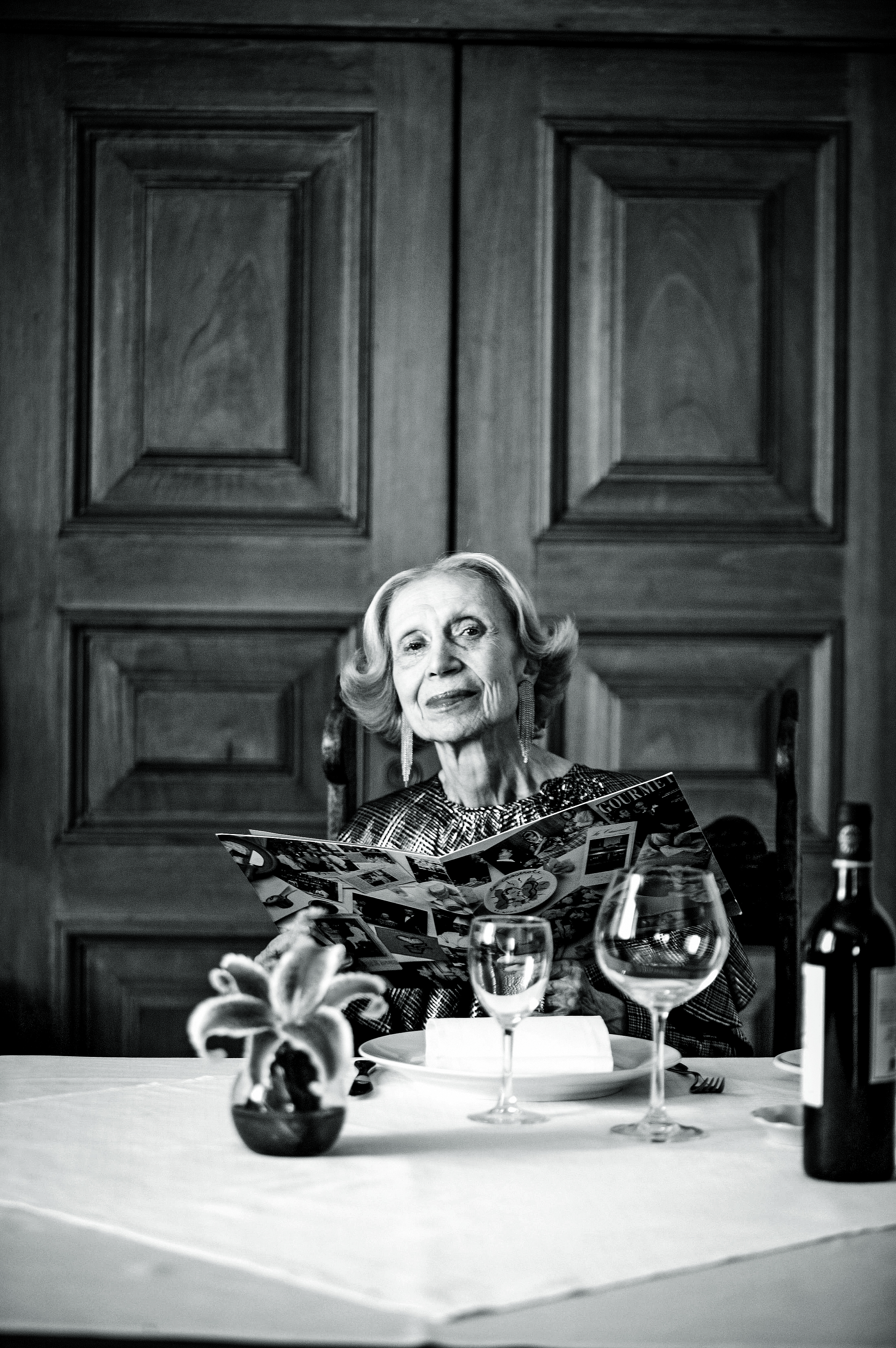 Foto preto e branco de Fortun&eacute;e Henry sentada &agrave; mesa segurando um card&aacute;pio.