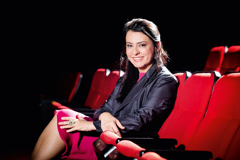 A imagem mostra Renata de Almeida sentada em uma poltrona de cinema.