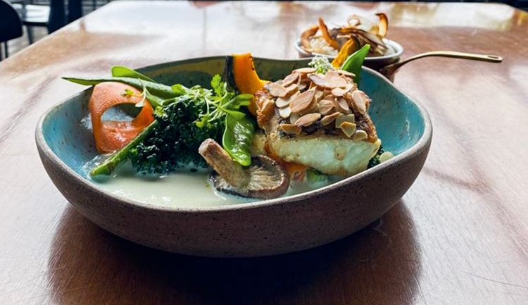 Peixe servido em um prato fundo de cerâmica junto de acompanhamentos, como o arroz de coco