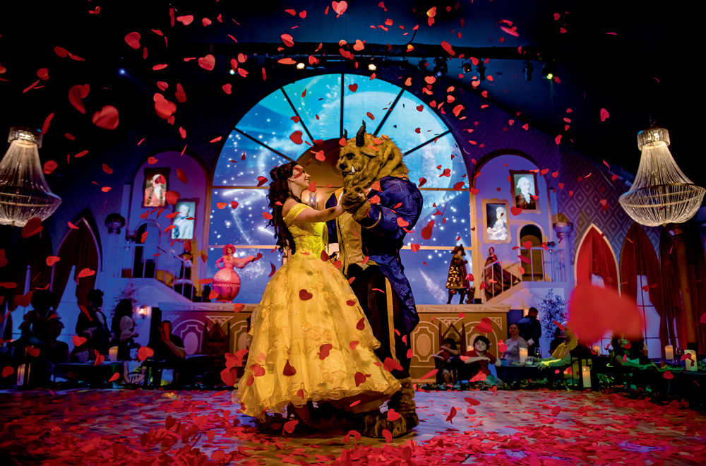a bela e a fera A imagem mostra a atriz da Bela e da Fera dançando no palco em uma chuva de pétalas de rosa.