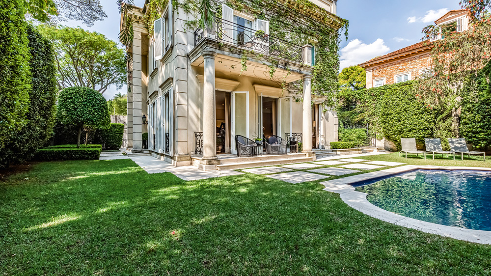 jovens-corretores-de-luxo-sp-Casa-Rua-Itália vista do jardim de casa com trepadeiras nas paredes. no jardim, há muito espaço de grama verde e uma piscina, à direita