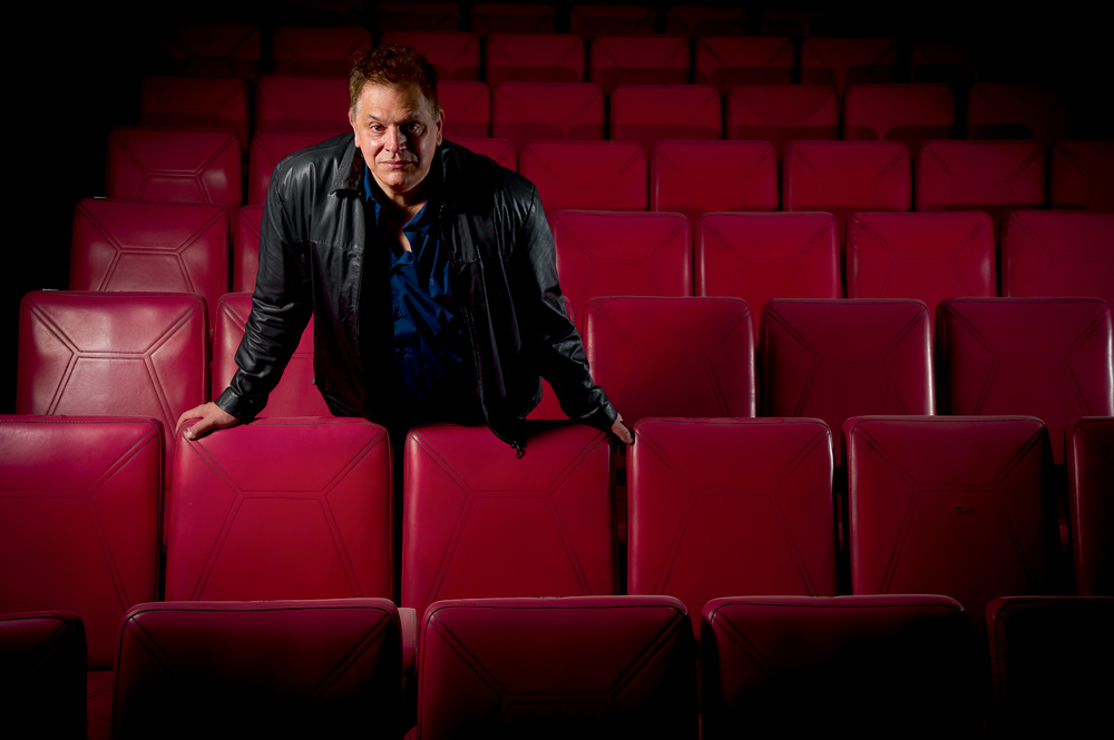reabertura-Cine-Bijou-Rodolfo-cadeiras.jpg rodolfo posando para a foto com expressão séria em meio a cadeiras da sala do cine bijou, encostado em algumas delas com os braços semiabertos