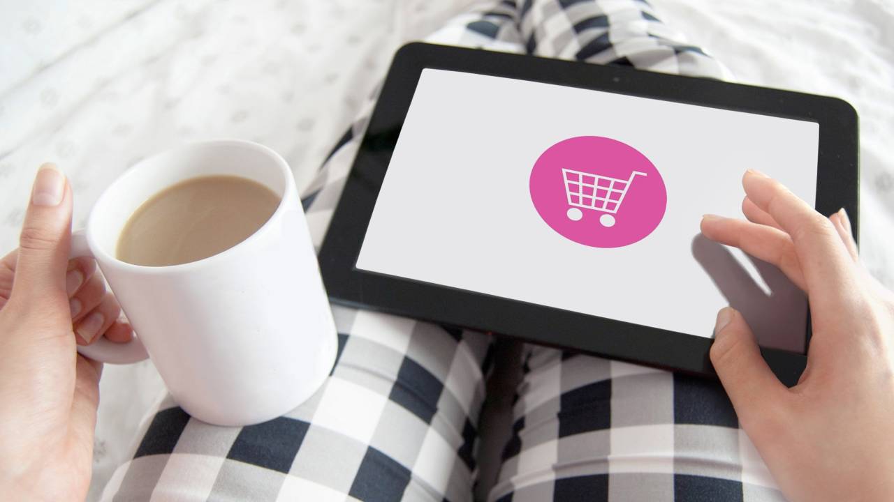Pessoa com um tablet no colo, no qual há uma tela, onde aparece um ícone de compra