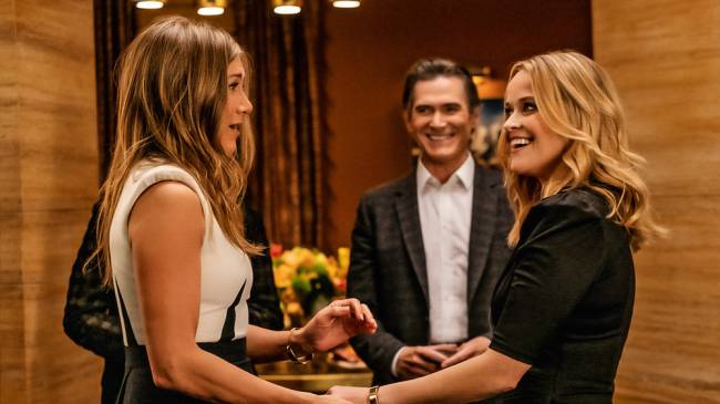 A imagem mostra Jennifer Aniston e Reese Witherspoon em cena de The Morning Show. Jennifer está com cara de surpresa enquanto aperta a mão de Reese.