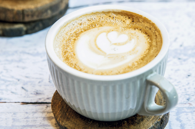 Xícara azul bebê sobre pires de madeira com latte dentro.