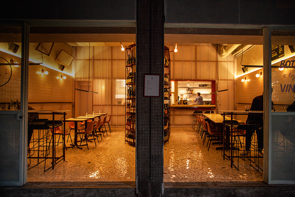 Ambiente do bar de vinhos Paloma, cujas paredes são forradas por azulejos de cor branca. Garrafas de vinho expostas pelo salão também fazem parte da decoração.