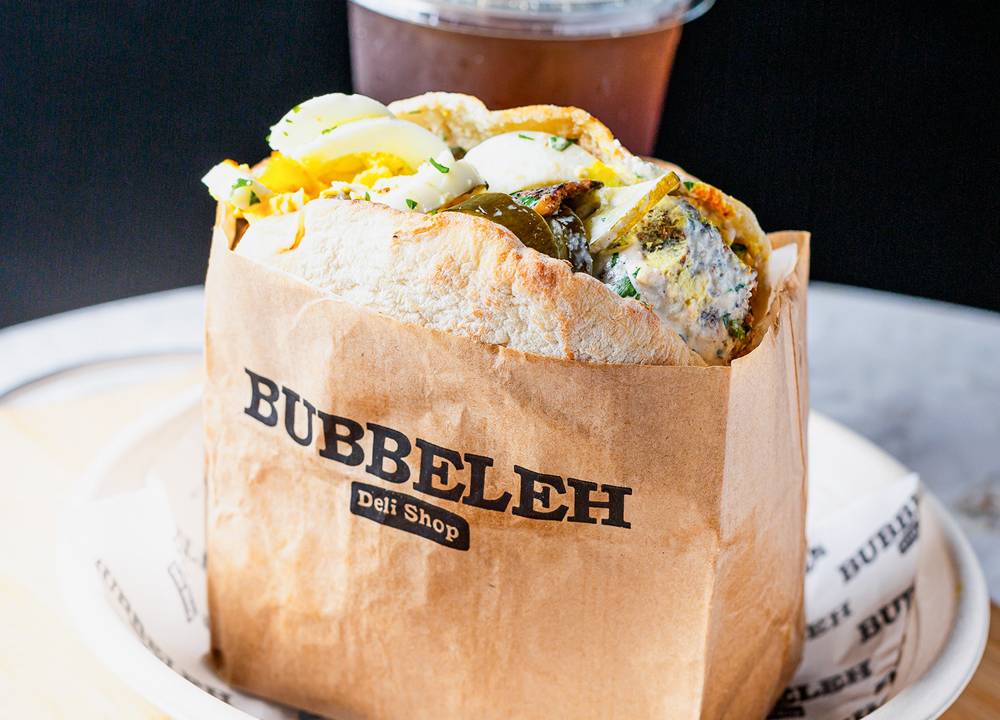 No pão sírio, lanche recheado por ovos cozidos, berinjela, falafel e mais é servido em um pequeno saco de papel com o logo da lanchonete