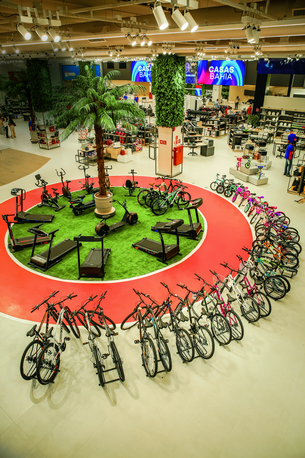 CASASBAHIA_16.JPG Foto tirada de um plano alto, mostra um gramado sintético em formato circular, rodeado por uma pista de corrida vermelha e por inúmeras bicicletas.
