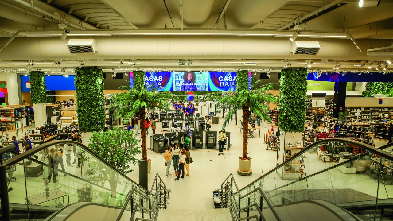 Foto tirada de cima de uma escada, mostrando todo interior da loja. Duas palmeiras ao centro e diversos estandes de produtos em volta.