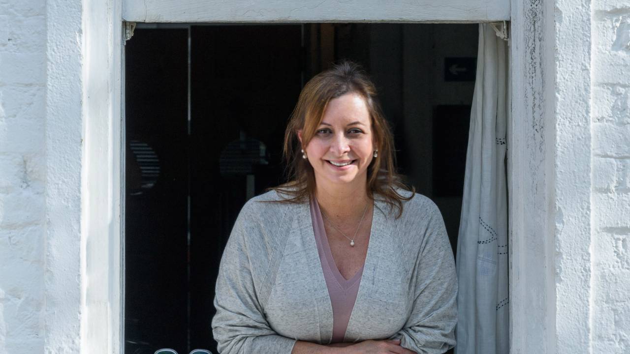 Carla Pernambuco sorri debruçada no parapeito de janela branca.