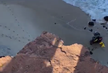 A imagem mostra a visão de cima da falésia, podendo ver a praia e o quadriciclo deitado na areia.