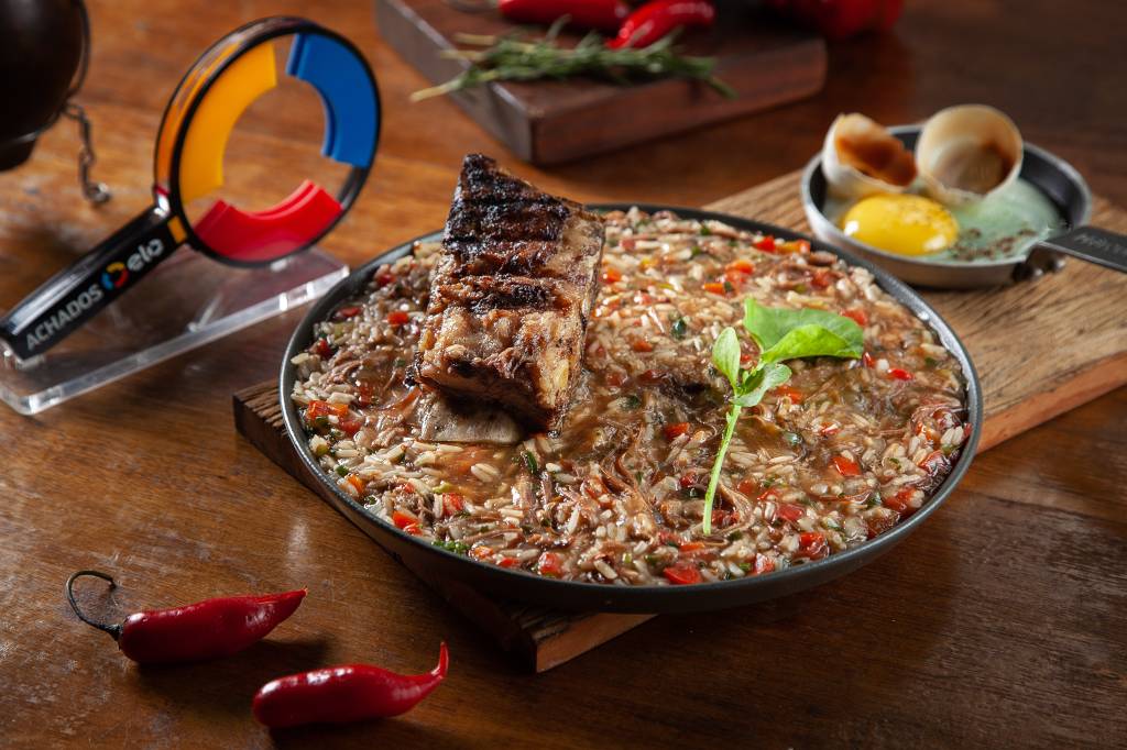 Arroz de costela com pedaço de costela por cima em panela de ferro sobre mesa de madeira.