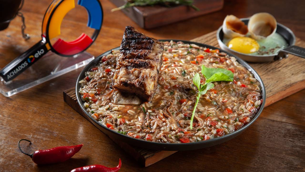 Arroz de costela com pedaço de costela por cima em panela de ferro sobre mesa de madeira.