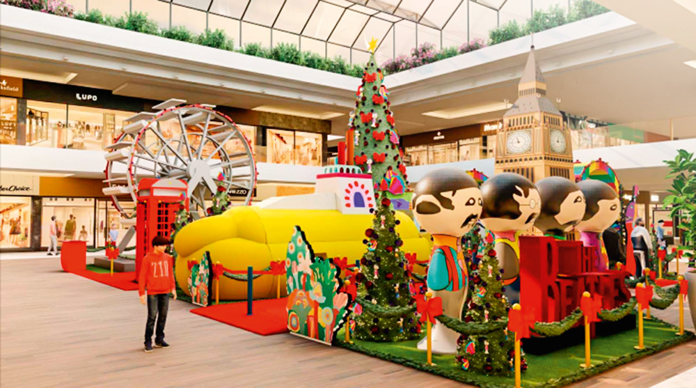 Um projeto mostra um espaço de decoração de Natal no shopping. Há árvores de Natal cercando o espaço, um Submarino Amarelo, quatro bonecos representando os Beatles, uma Roda-Gigante, o Big Ben de Londres e outras atrações