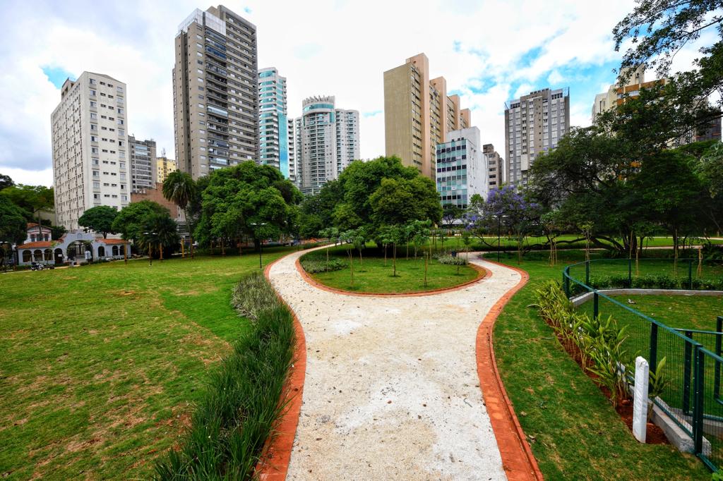 Via com chão branco aparece no meio de um gramado com prédios no horizonte.