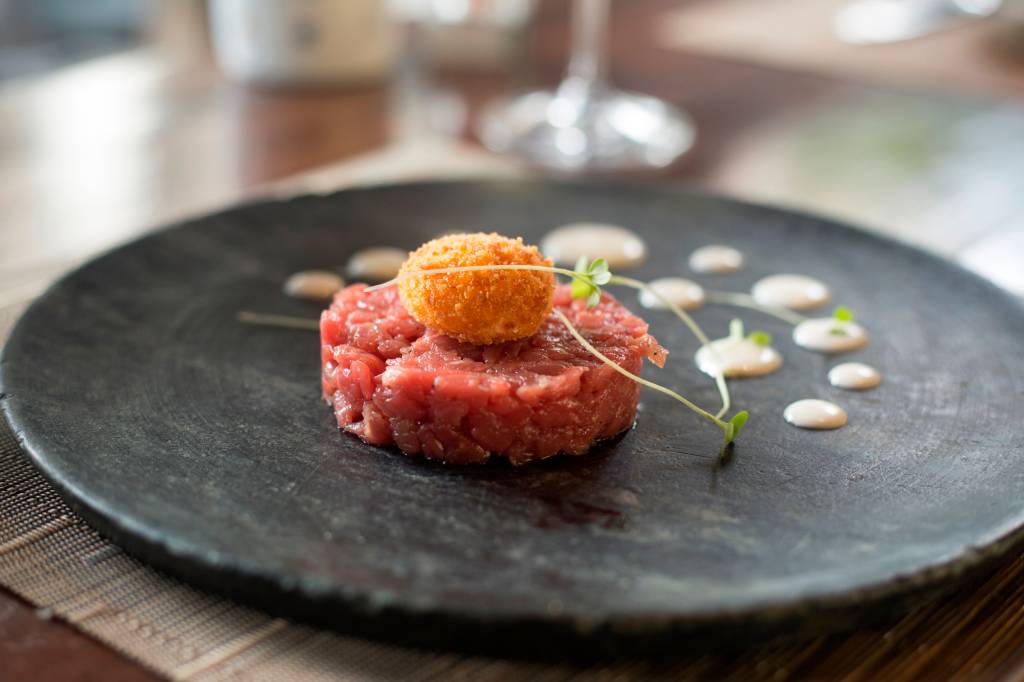 Settimana della Cucina Regionale Italiana Tartare de carne sobre prato de pedra cinza com gema de ovo frito por cima,