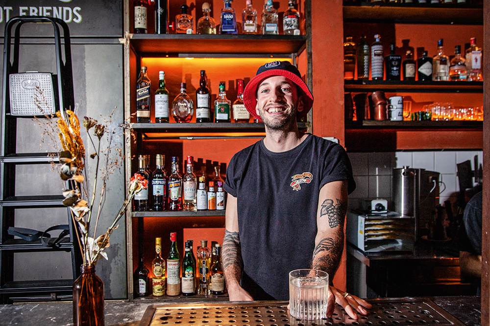 Retrato do bartender Lula Mascella_3.jpg Rapaz de gorro em balcão de bar com drinque na mão
