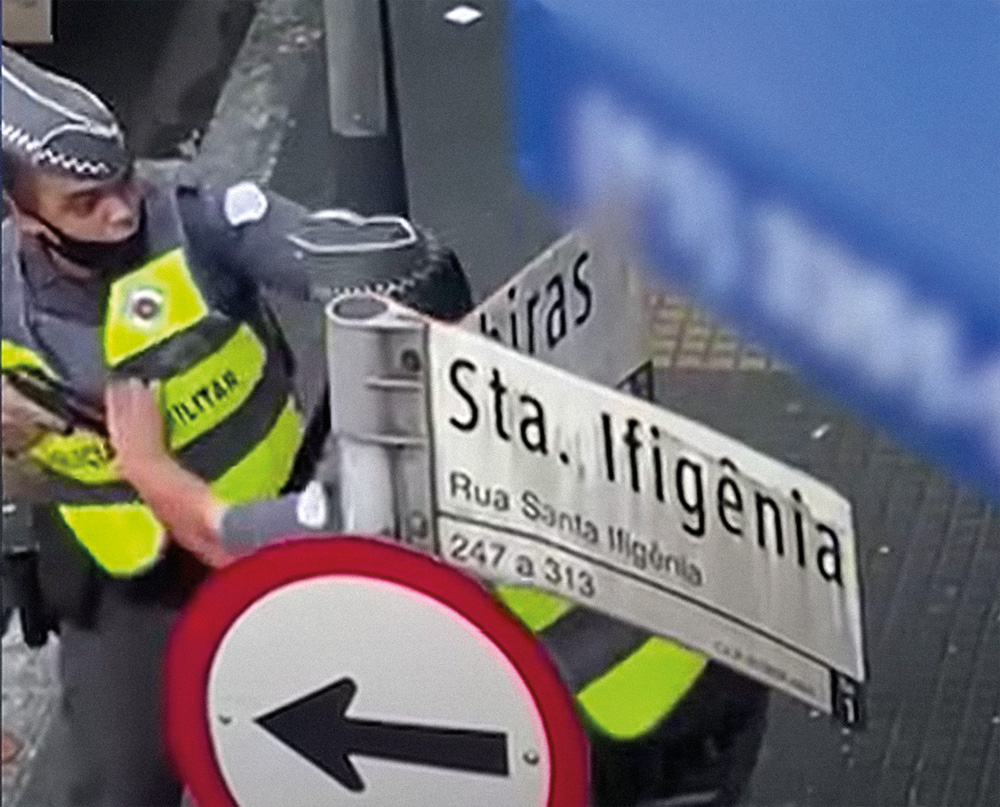 Policial aponta arma para outro A foto mostra um PM agindo contra o outro, na tentativa de desarmar o que estava apontando uma arma para a sua cabeça. A foto é de cima e dá para ver a placa da rua