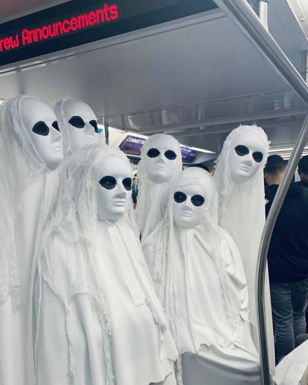 SubwayCreatures fantasmas A imagem mostra seis pessoas em fantasias de fantasma. Estão vestidas inteiras com um pano branco e nos olhos há uma maquiagem preta.