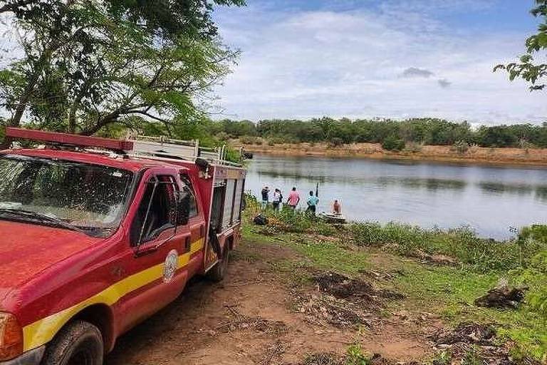 A imagem mostra a beira de um rio e com um carro do corpo de bombeiros em destaque.
