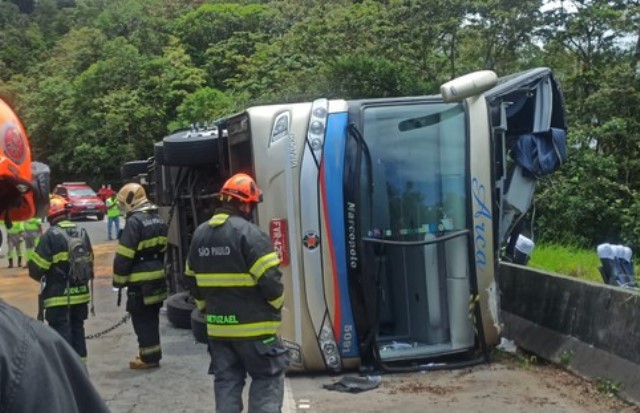 Ônibus tombado em rodovia, rodeado por bombeiros.