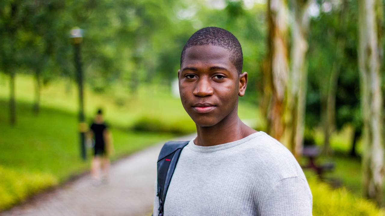A imagem mostra um jovem negro com uma mochila no ombro