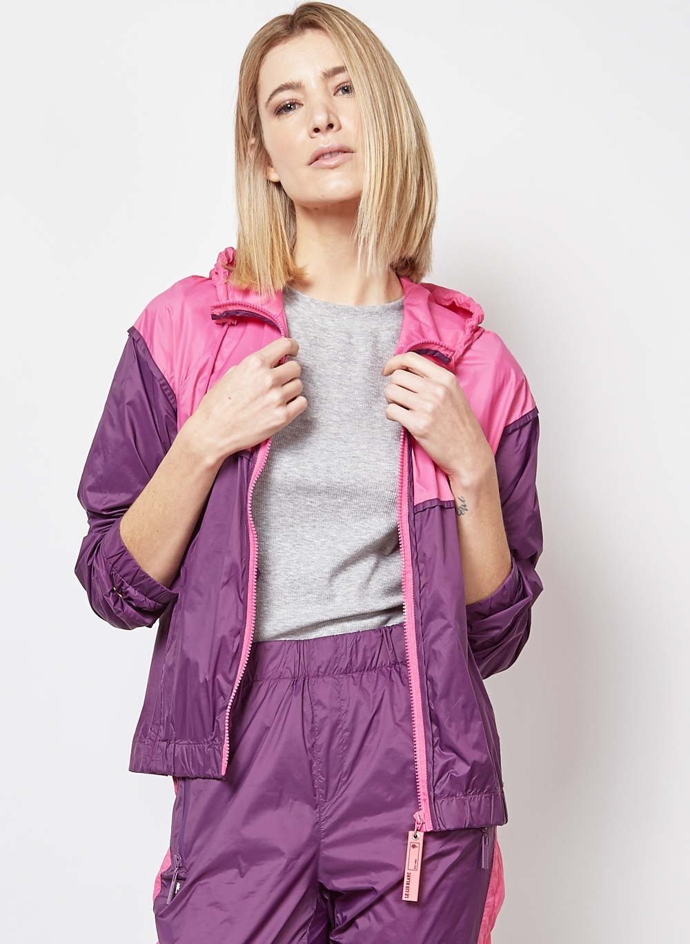jaqueta Uma mulher loira posa vestindo um conjunto de jaqueta e calça de nylon roxo com detalhes em rosa