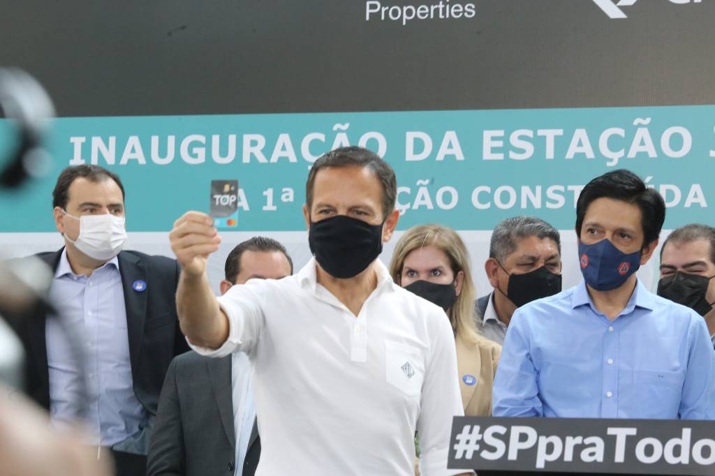 joão-doria-inaugura-cartão-top-benefício-mobilidade joão doria cercado por pessoas e pelo prefeito Ricardo Nunes erguendo com a mão direita o cartão top