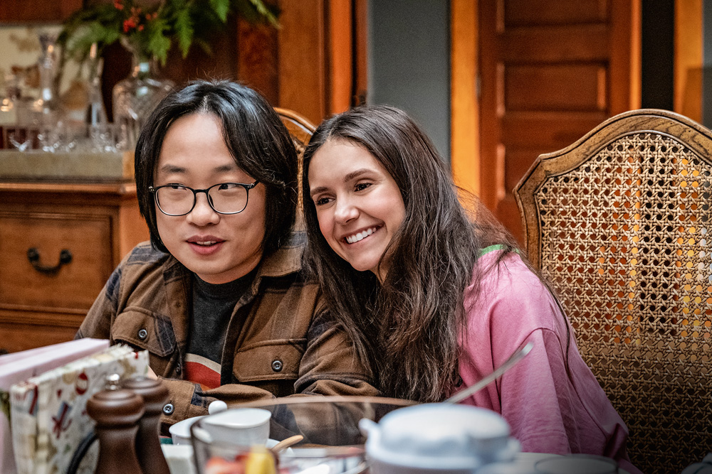 Imagem mostra um homem e uma mulher sorrindo sentados em cadeiras de madeira.