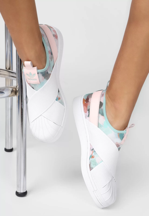 tenis adidas Foto mostra o pé de uma pessoa vestindo um tênis branco, rosa e azul